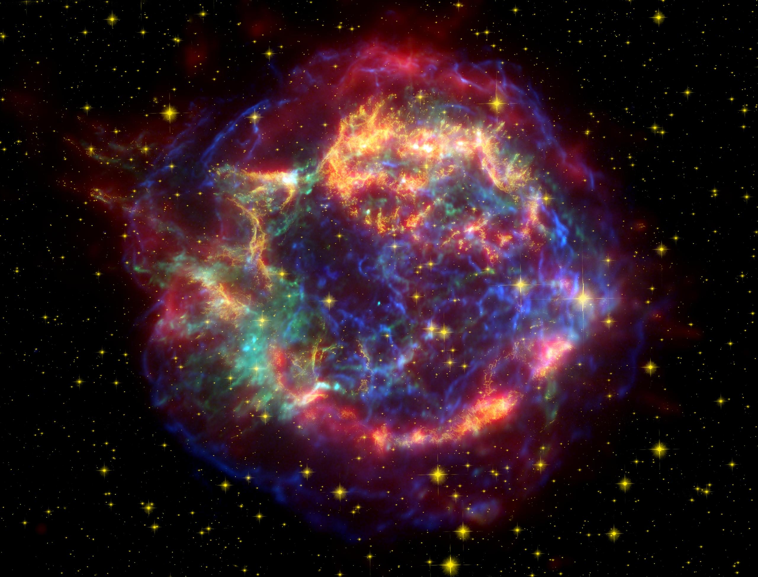 A false color image composed of data from three sources: Red is infrared data from the Spitzer Space Telescope, gold is visible data from the Hubble Space Telescope, and blue and green are data from the Chandra X-ray Observatory. The small, bright, baby-blue dot just off-center is the remnant of the star's core.